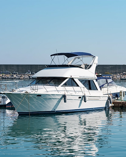 White motor yacht moored in a calm harbor, blue sky above and a blue canopy on the upper deck.