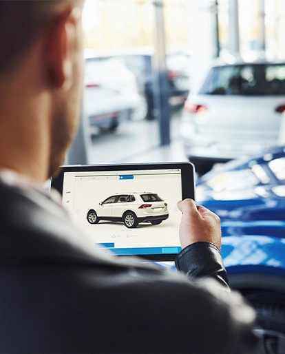 Man at a car dealership using a tablet to view a white SUV on screen.